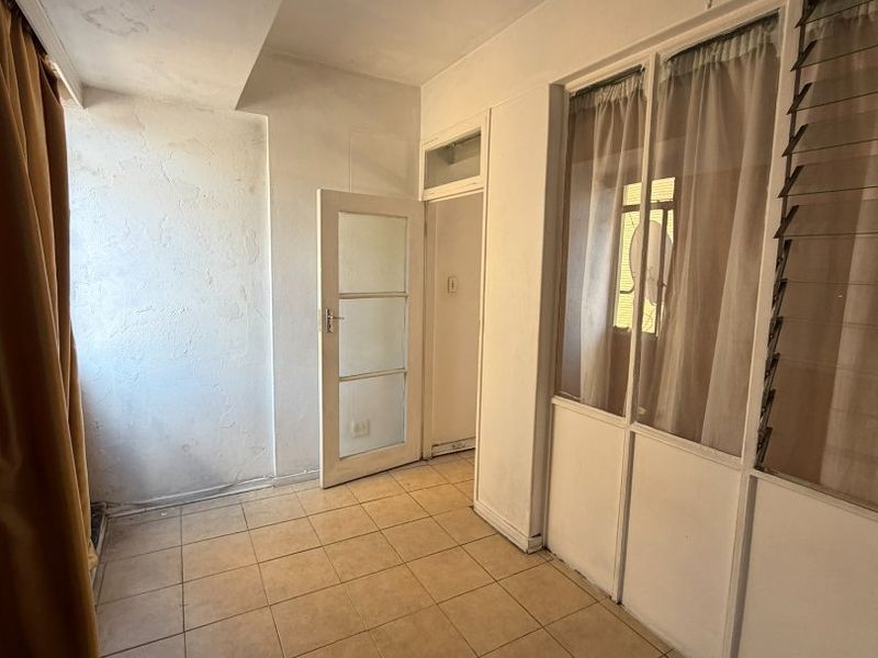 An enclosed balcony or sunroom featuring tiled flooring, louvre windows, and a glass panel door, requiring cosmetic updates to the wall finishes.
