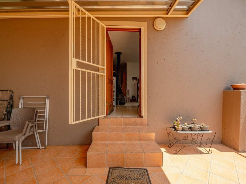 A covered patio area featuring tiled flooring, steps leading to the entrance, and a security gate, providing a functional outdoor transition space.