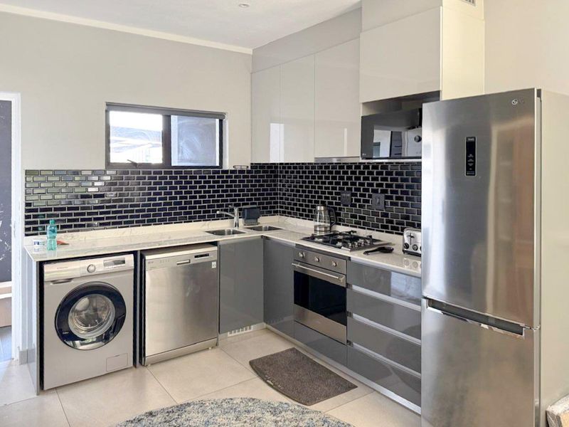Modern kitchen featuring glossy grey and white cabinetry, black subway tile backsplash, stone countertops, and integrated stainless steel appliances.