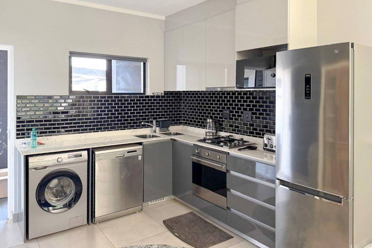 Modern kitchen featuring glossy grey and white cabinetry, black subway tile backsplash, stone countertops, and integrated stainless steel appliances.