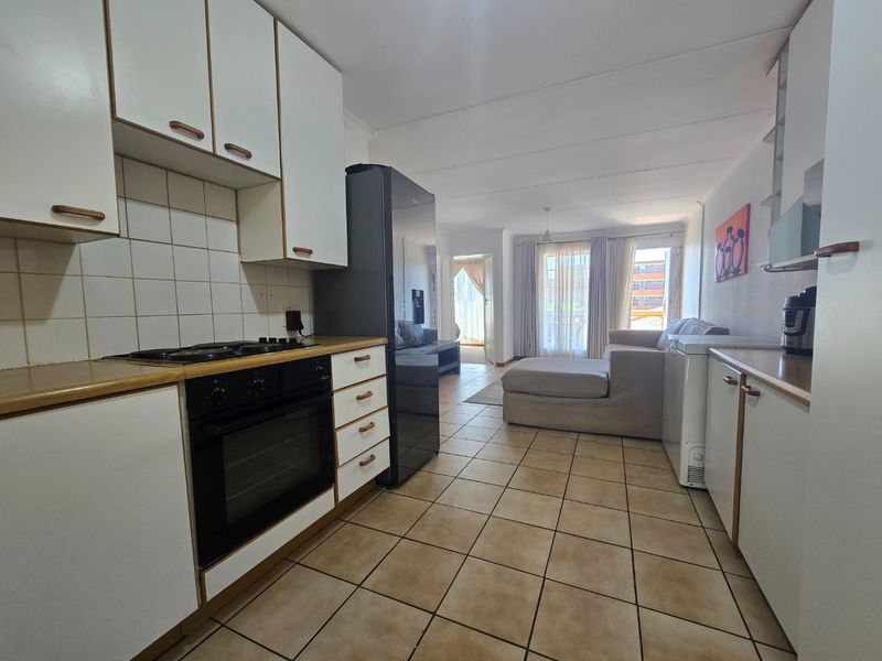 Open-plan kitchen and living area featuring tiled flooring, built-in cabinetry, and integrated cooking appliances, leading to a bright lounge space.