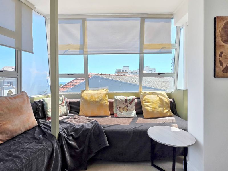 Enclosed balcony area featuring large windows with roller blinds, offering natural light and views of the surrounding neighborhood.