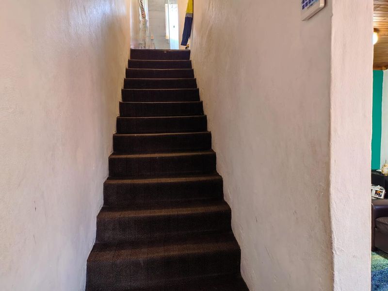 A narrow interior staircase featuring dark carpeted steps and plain white walls leading to an upper level.