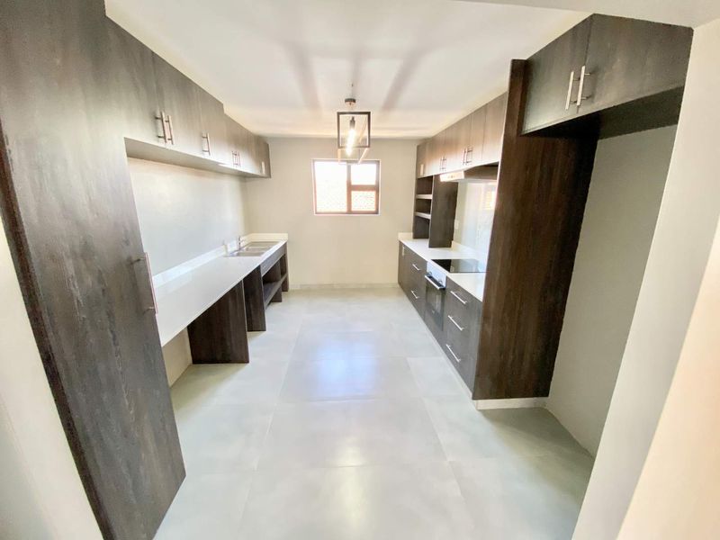 Modern galley-style kitchen featuring dark wood cabinetry, stone countertops, integrated oven and hob, and large format floor tiles.