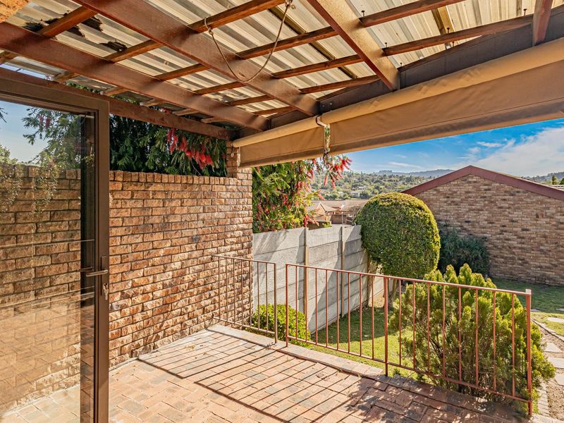 Covered patio area featuring brick paving, a timber pergola with corrugated roofing, and a retractable awning, overlooking a private garden space.