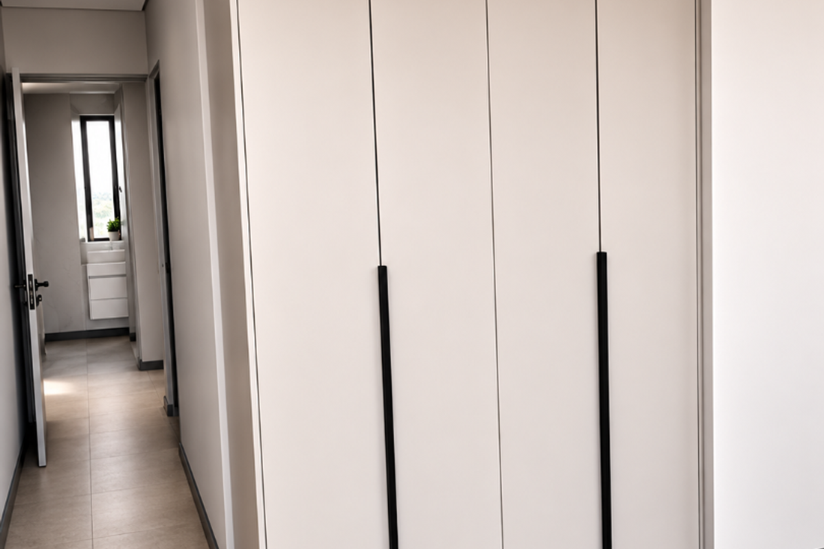 A modern bedroom featuring sleek, floor-to-ceiling built-in cupboards with matte black handles, neutral tiled flooring, and recessed downlighting.