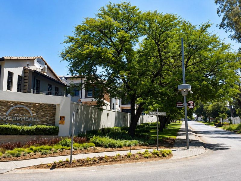 Street view of the Goedehemel estate entrance, featuring a stone-clad boundary wall, landscaped verge, and paved sidewalk along the road.