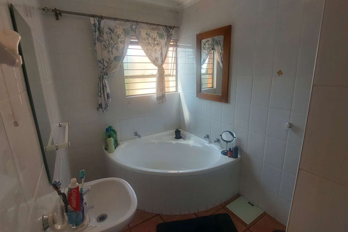 A functional bathroom featuring a corner bathtub, wall-mounted basin, and tiled walls.
