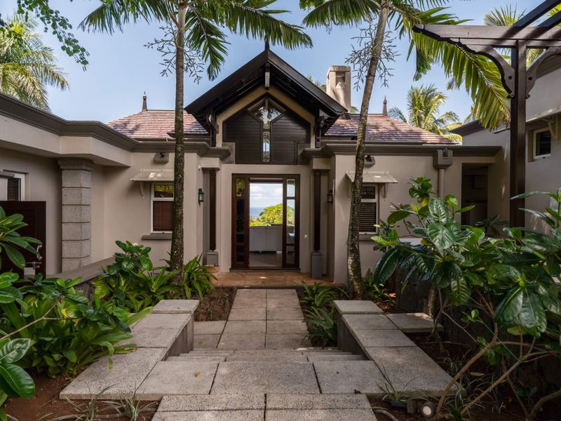 A beautifully maintained front entrance featuring a stone pathway, timber-framed doorway, and architectural roof detailing, surrounded by lush tropical landscaping.