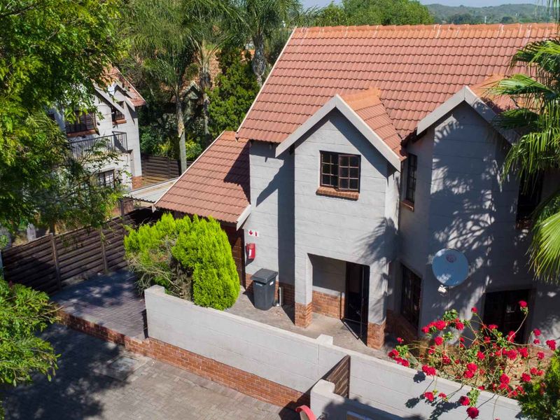 Aerial view of a two-story townhouse featuring a tiled roof, brick boundary wall, and paved driveway within a landscaped residential setting.