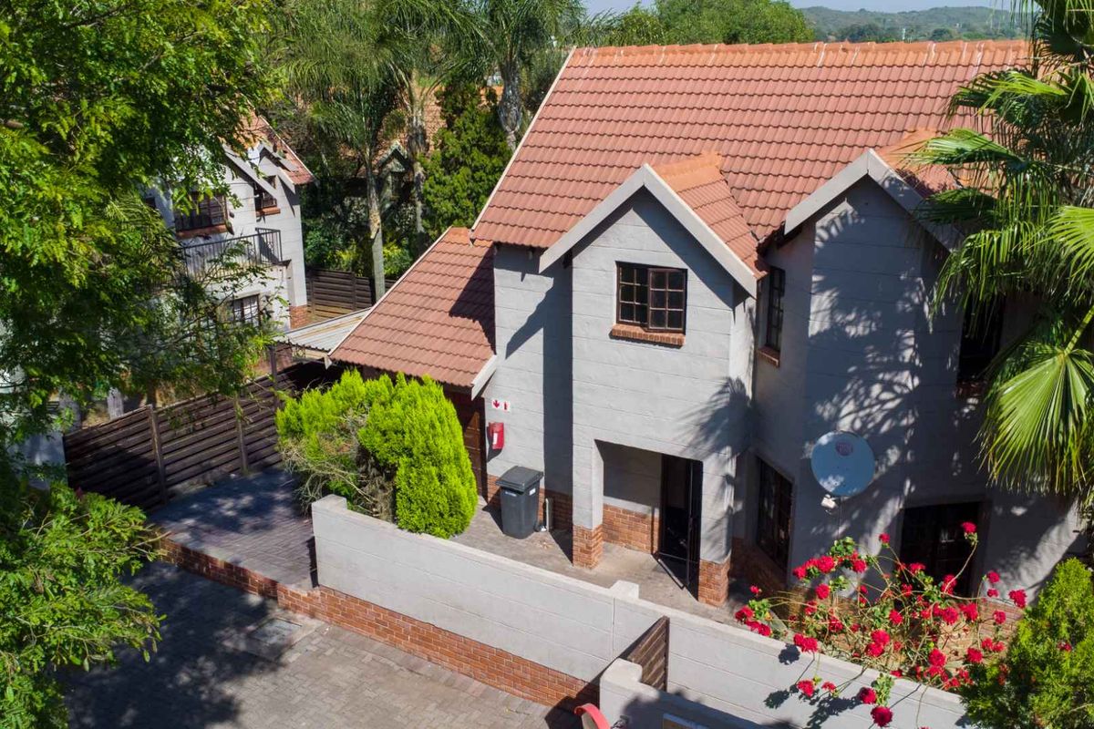 Aerial view of a two-story townhouse featuring a tiled roof, brick boundary wall, and paved driveway within a landscaped residential setting.