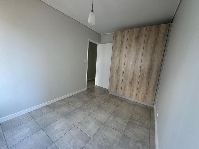 A clean, empty bedroom featuring modern grey floor tiles and light wood-finish built-in cupboards.