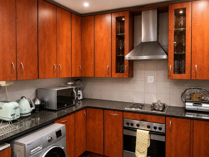A functional kitchen featuring warm-toned wooden cabinetry, granite countertops, a tiled backsplash, and integrated stainless steel appliances including an oven and extractor fan.
