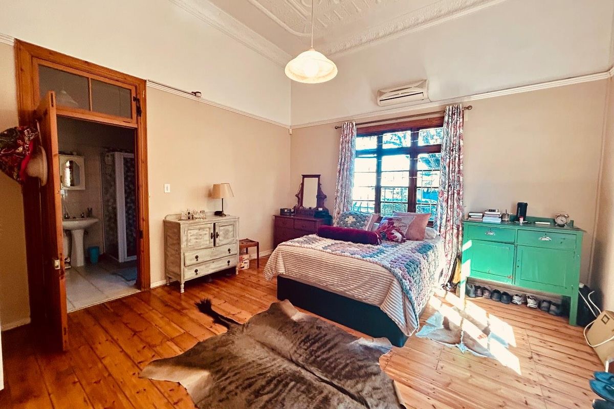 Spacious bedroom featuring original timber flooring, ornate ceiling detailing, and an en-suite bathroom, complemented by a wall-mounted air conditioning unit.