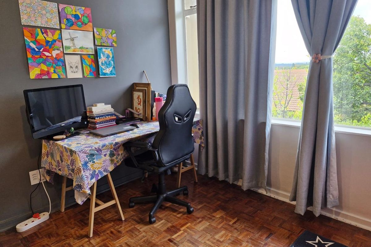 A bedroom or home office space featuring classic parquet flooring, a large window with natural light, and a dark accent wall.