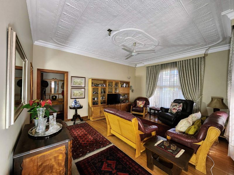 Spacious living room featuring a classic pressed metal ceiling with a decorative ceiling rose, hardwood flooring, and traditional timber door frames.