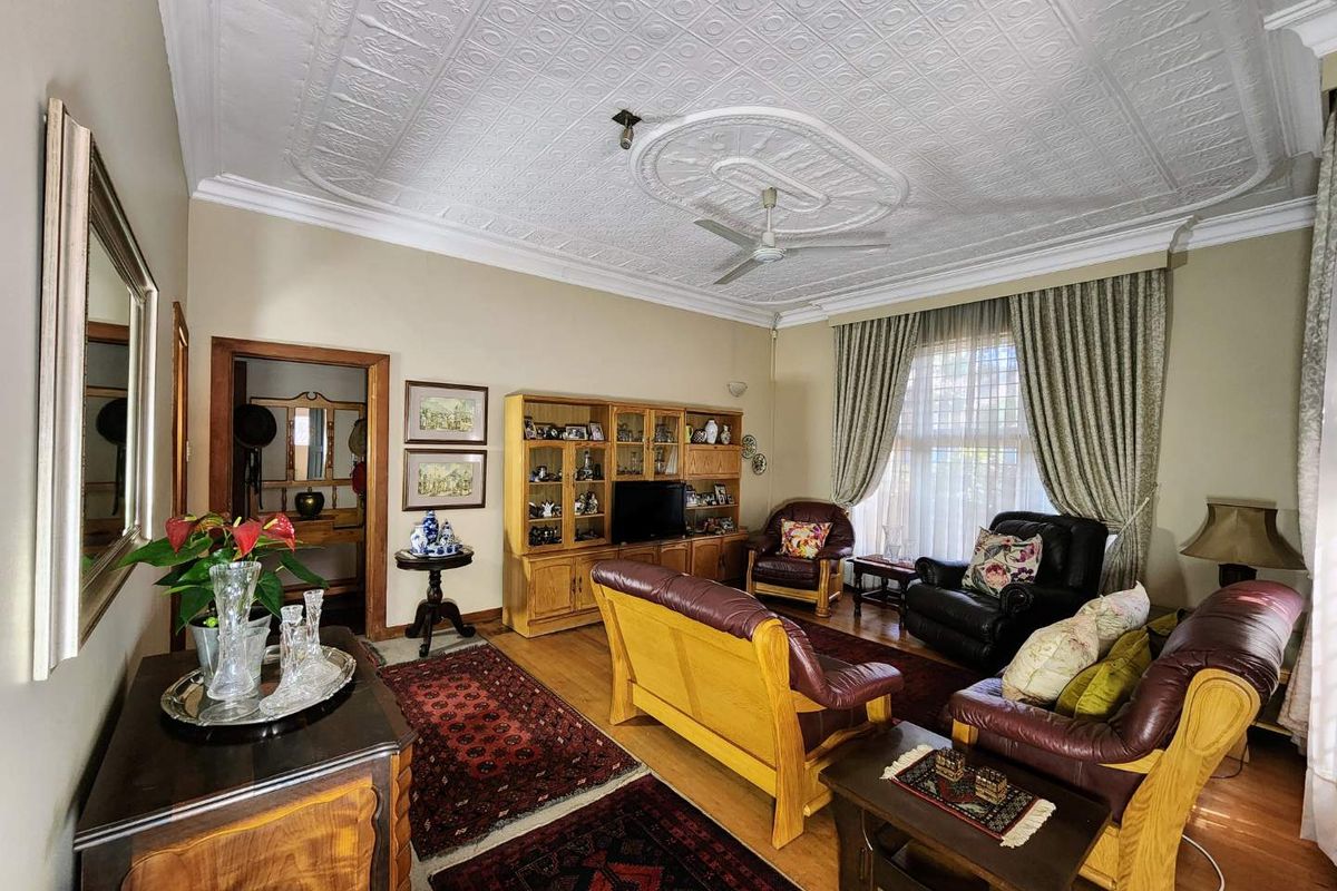 Spacious living room featuring a classic pressed metal ceiling with a decorative ceiling rose, hardwood flooring, and traditional timber door frames.