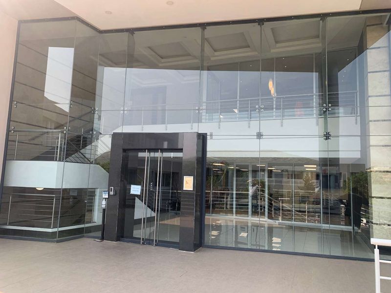 Modern office building entrance featuring a prominent glass facade, polished stone door frame, and a spacious, light-filled lobby area.