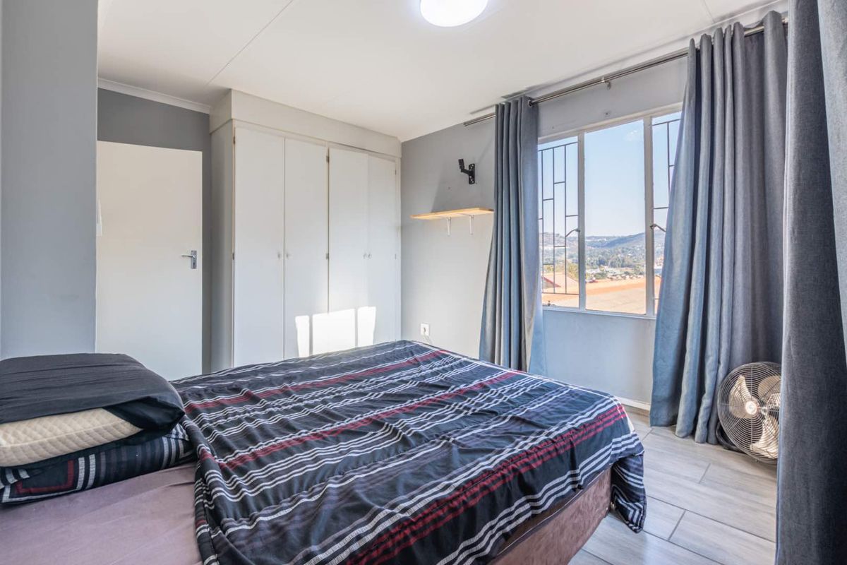 A bedroom featuring built-in cupboards, tiled flooring, and a window with security bars offering an elevated view.
