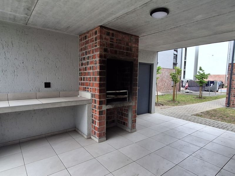 Covered patio area featuring a built-in brick braai, concrete prep counter, and tiled flooring, overlooking a communal garden space.