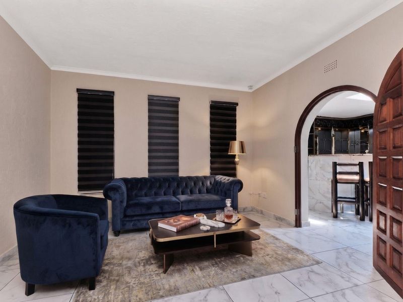 A well-maintained living room featuring marble-look floor tiles, an elegant arched doorway leading to an adjacent space, and modern zebra blinds.