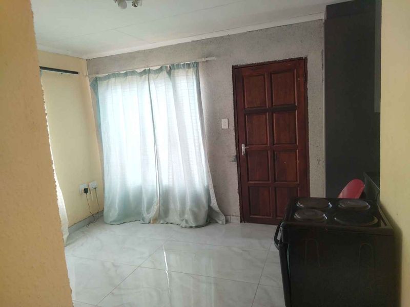 An open-plan living area featuring tiled flooring and a timber door, requiring cosmetic updates to improve the overall finish and aesthetic appeal.