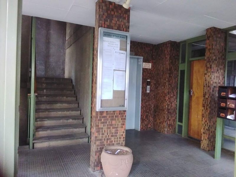 Communal apartment building entrance lobby featuring a staircase, elevator access, and wall-mounted mailboxes with dated mosaic tile finishes.