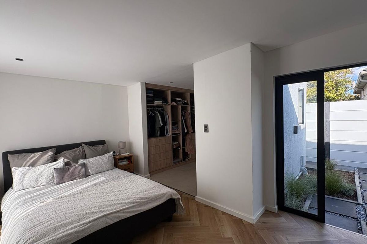 Modern bedroom featuring herringbone timber flooring, built-in wooden cabinetry, and a large glass sliding door providing direct access to a private outdoor courtyard.
