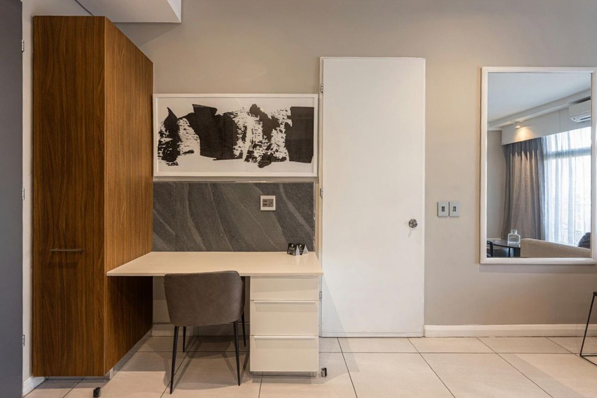 A well-maintained bedroom featuring a built-in wooden wardrobe, integrated desk with stone splashback, and neutral tiled flooring.
