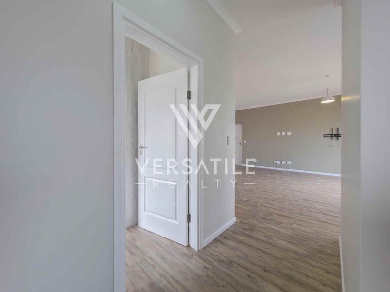A bright, empty hallway featuring modern laminate flooring and clean white door frames, leading into an open-plan living area.