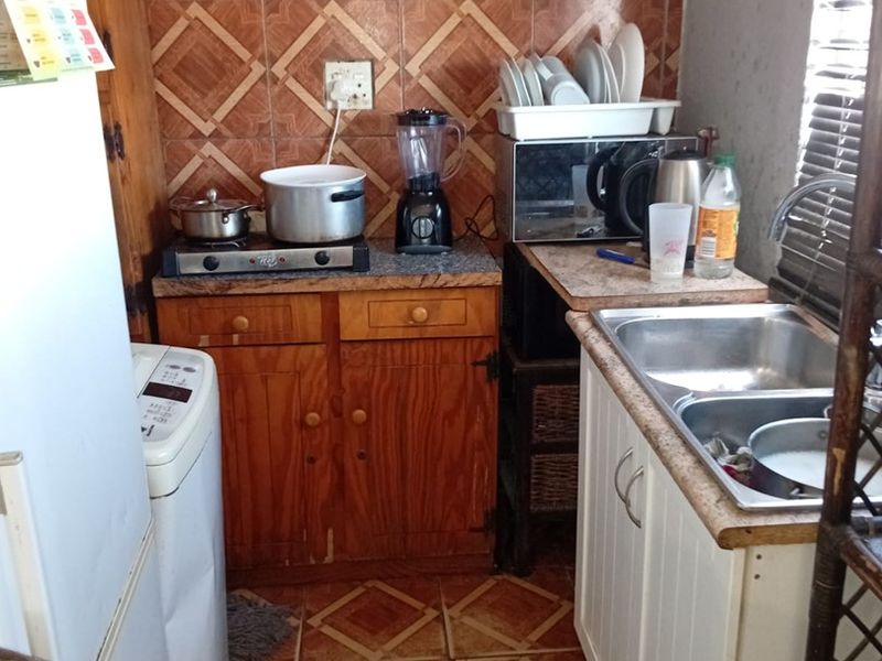 A compact kitchen featuring wooden cabinetry, laminate countertops, a double bowl stainless steel sink, and patterned wall and floor tiles.
