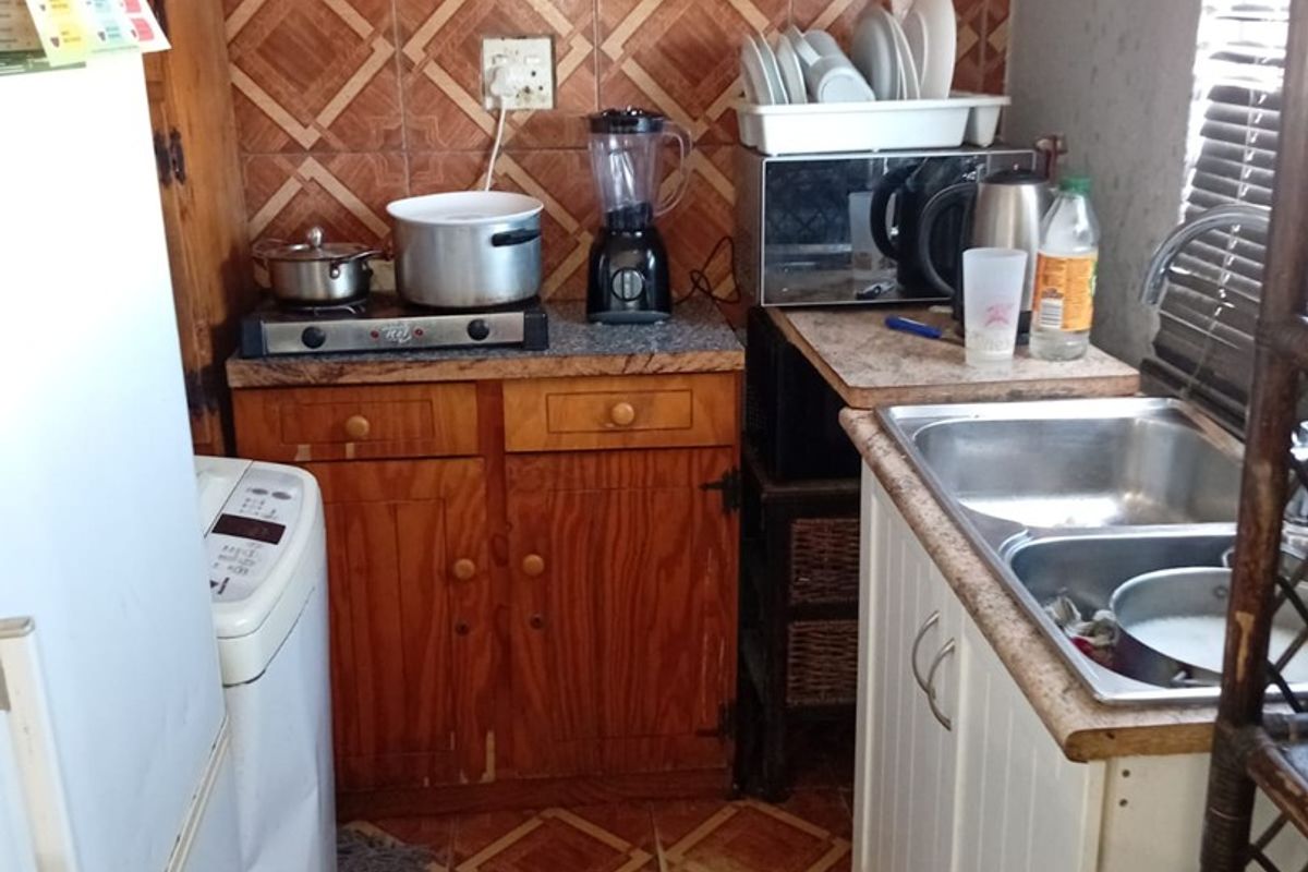 A compact kitchen featuring wooden cabinetry, laminate countertops, a double bowl stainless steel sink, and patterned wall and floor tiles.