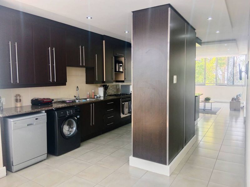 Modern open-plan kitchen featuring dark wood cabinetry, granite countertops, and integrated appliances, flowing into a bright living area with large windows.