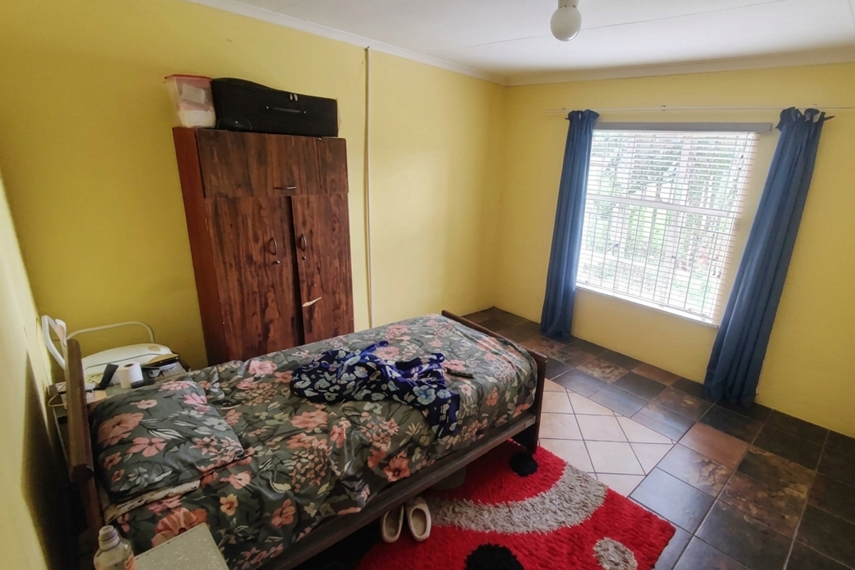 A bedroom featuring tiled flooring and a window with fitted blinds, providing a functional space with potential for cosmetic updates.