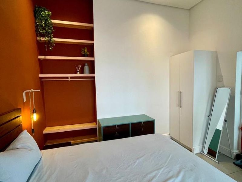 A bedroom featuring a bold accent wall, built-in wooden shelving, and a white built-in wardrobe with recessed ceiling lighting.