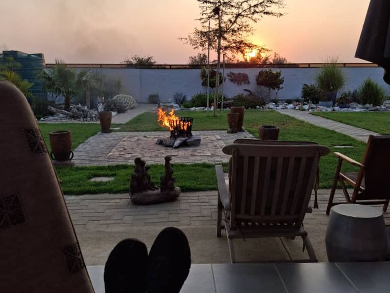 A covered patio area overlooking a landscaped garden with a brick fire pit and perimeter wall at sunset.