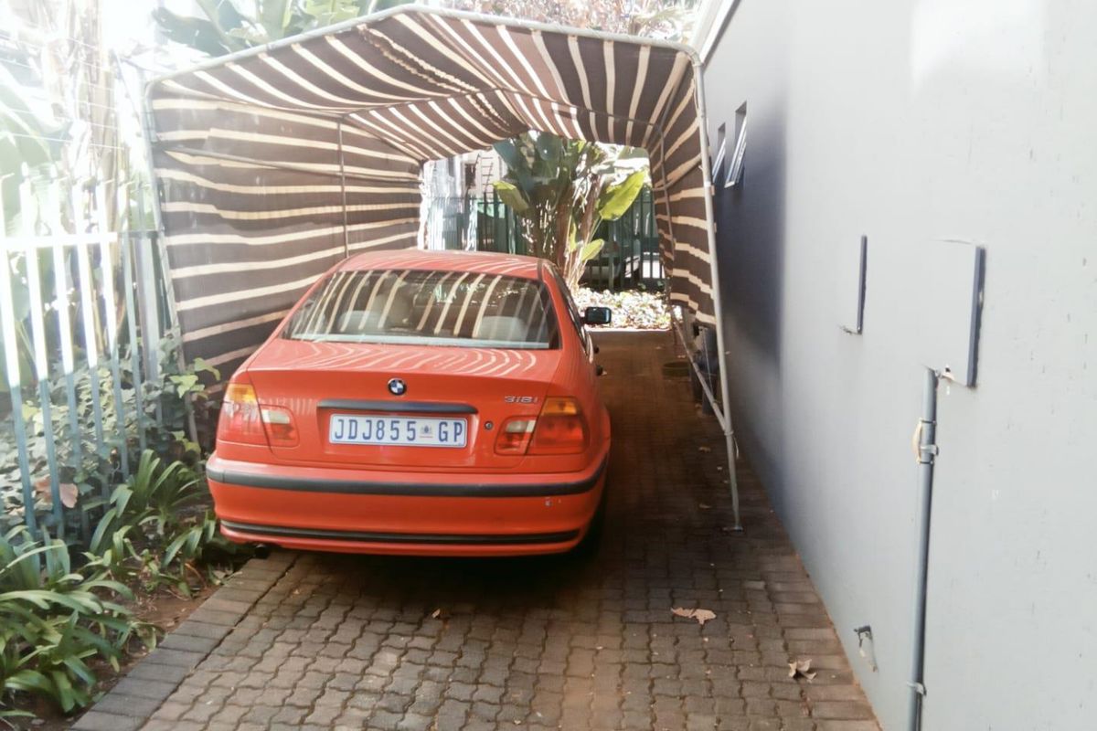 A paved driveway area featuring a temporary shade cloth carport structure alongside the building exterior.