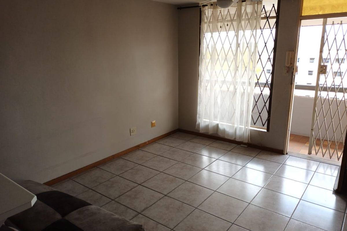 An empty living room featuring tiled flooring, a ceiling fan, and direct access to a balcony through a security gate and sliding door.