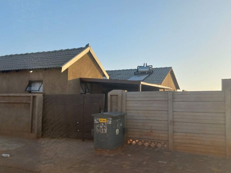 Front exterior view of the property featuring a tiled roof, solar water heater, precast concrete boundary wall, and a sliding gate.