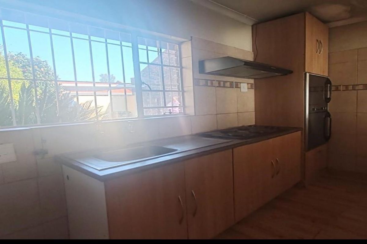 A functional kitchen featuring built-in cabinetry, a hob, extractor fan, and integrated oven, with a window providing natural light and security bars.