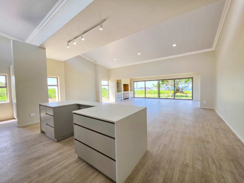 Spacious open-plan living area featuring a modern kitchen island, vaulted ceilings with recessed lighting, and large sliding glass doors leading to the outdoors.
