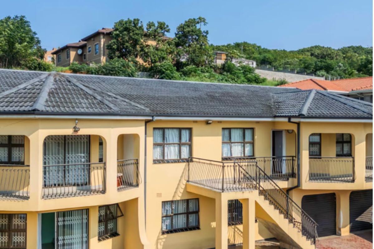 Rear view of a multi-level residential property featuring balconies, an external staircase, paved patio areas, and integrated garage access.