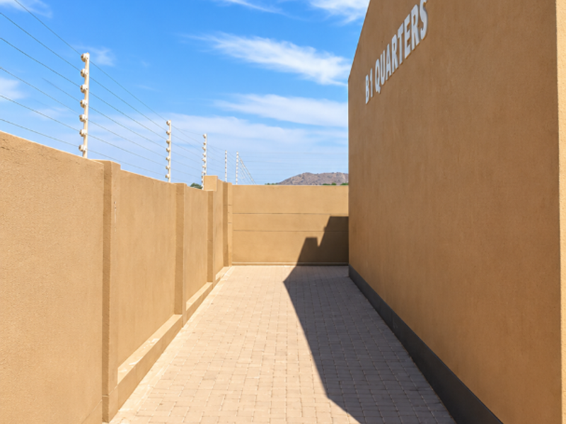 A clean, paved exterior walkway alongside a perimeter wall with electric fencing, providing access to the B1 Quarters area.