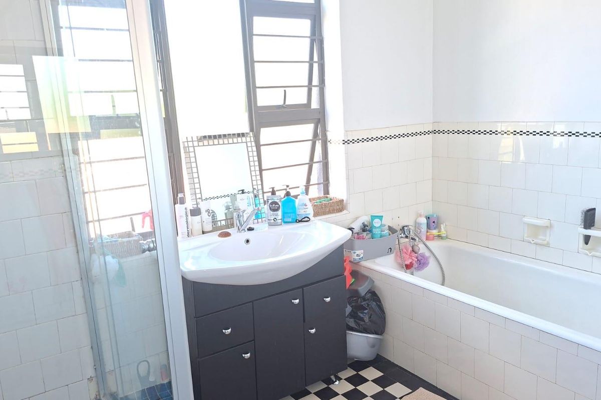 A functional bathroom featuring a vanity basin, a bathtub with shower mixer, and classic black and white tiled flooring.