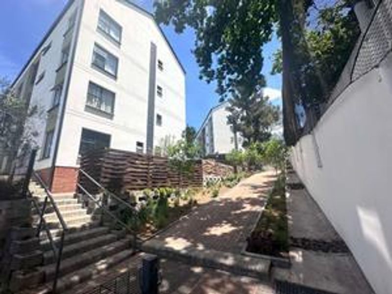 Exterior view of the townhouse complex featuring a paved walkway, concrete stairs with metal handrails, and landscaped retaining walls.