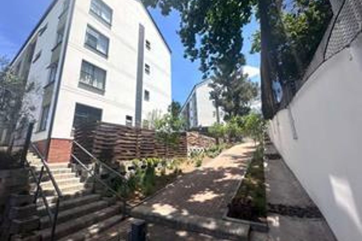 Exterior view of the townhouse complex featuring a paved walkway, concrete stairs with metal handrails, and landscaped retaining walls.