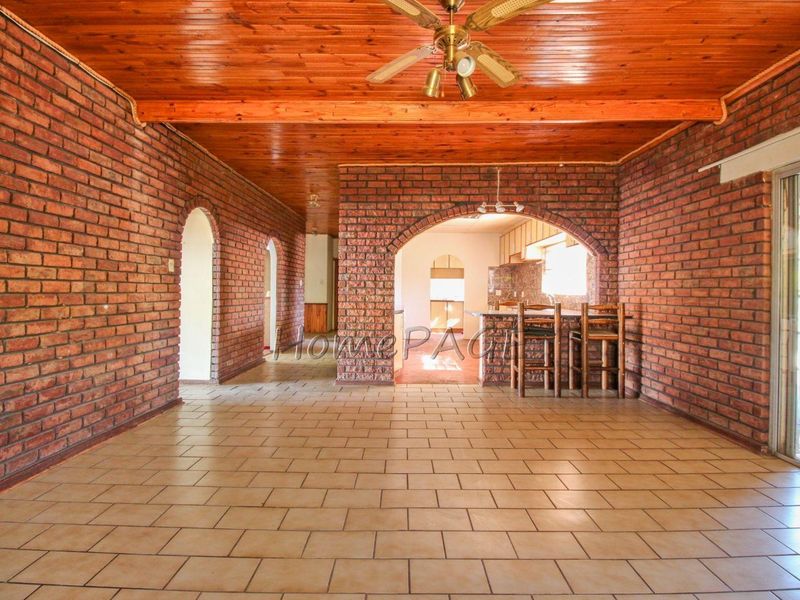 Spacious open-plan living area featuring exposed brick walls, timber ceiling, and tiled flooring, with a breakfast bar connecting to the kitchen area.