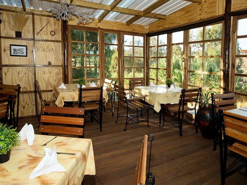 A rustic dining area featuring timber wall paneling, wooden flooring, and large timber-framed windows that provide ample natural light and garden views.