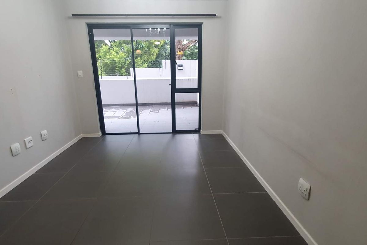 An empty living room featuring large format floor tiles, neutral walls, and a sliding glass door providing access to an outdoor balcony area.