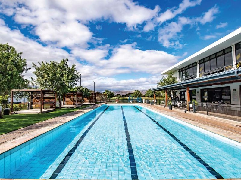 A well-maintained outdoor swimming pool area featuring a lap pool, timber pergolas, and a covered patio space adjacent to the building.